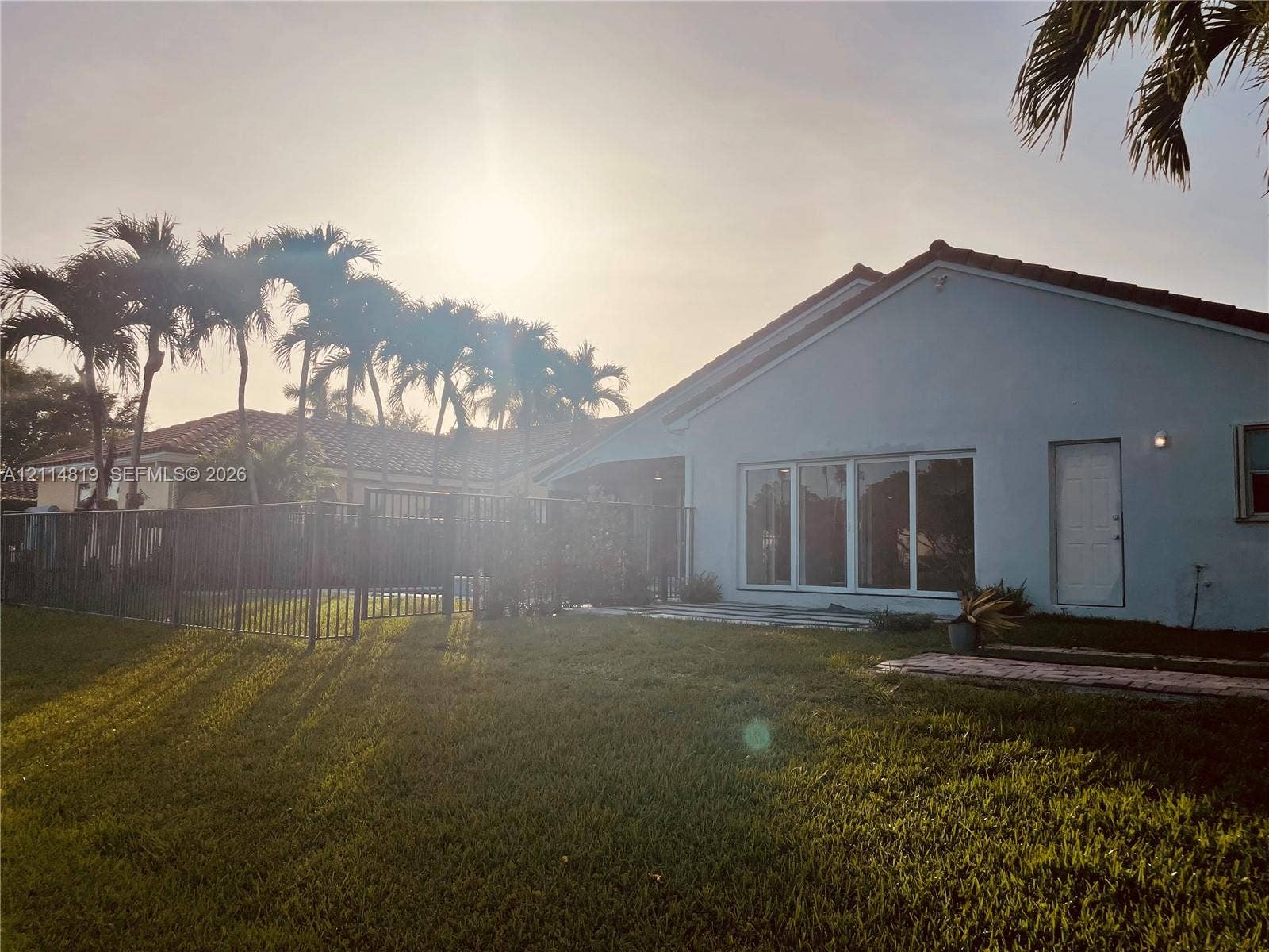 1952 Water Ridge Drive, #1952, Weston, Weston, FL 33326 Exterior rear elevation featuring a concrete patio, metal perimeter fencing, tiled roof, and mature palm trees