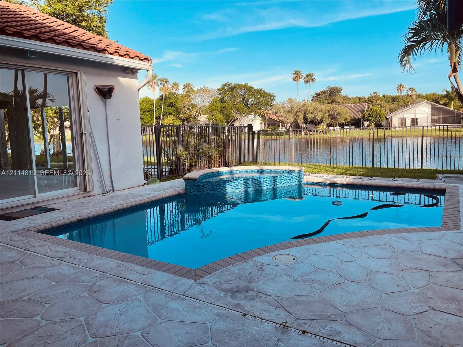 1952 Water Ridge Drive, #1952, Weston, Weston, FL 33326 In-ground swimming pool with an attached raised spillover spa, tiled water line, concrete paver decking, and metal perimeter fencing overlooking a pond