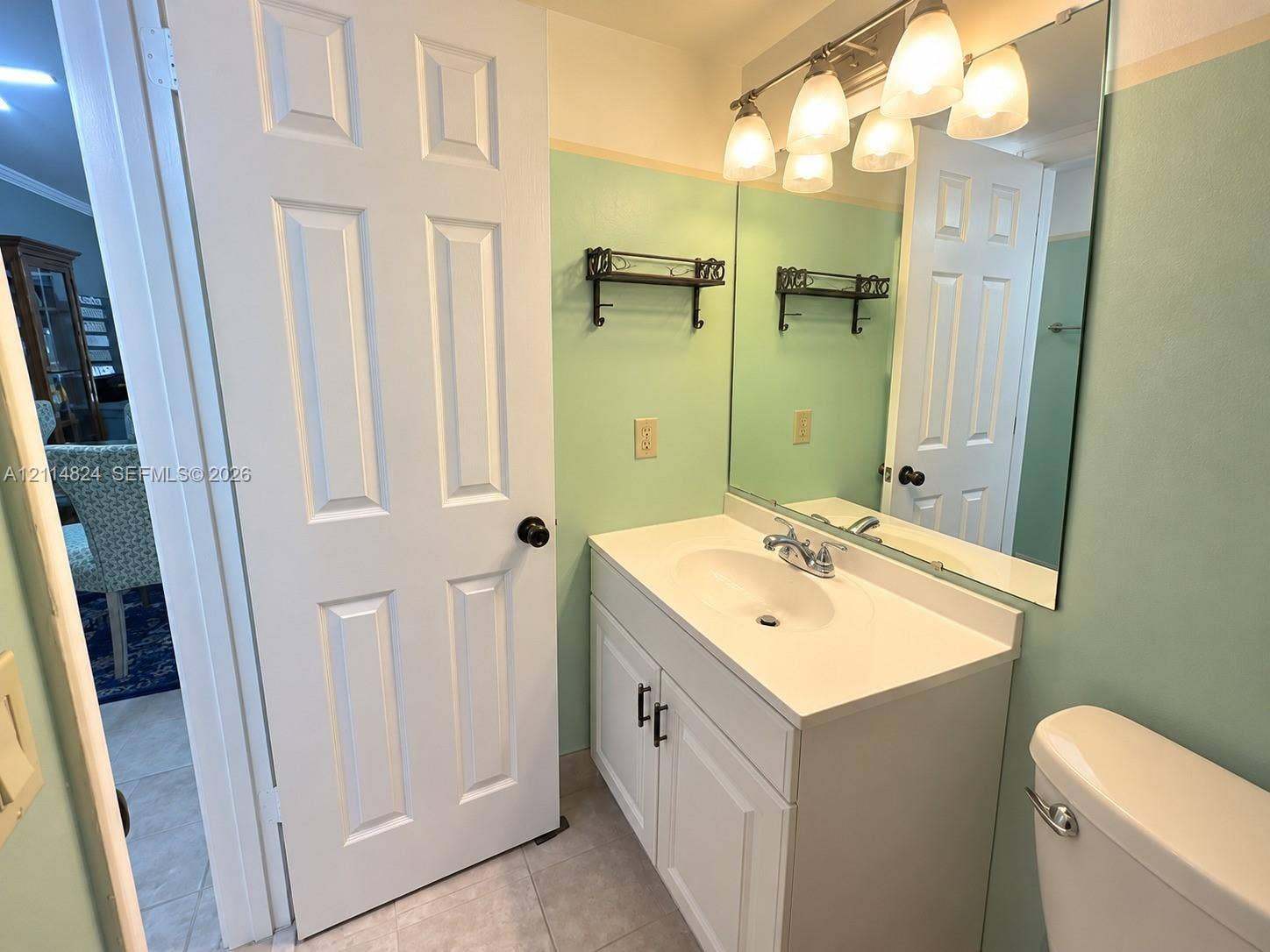 563 Durham T, #563, Deerfield Beach, FL 33442 White vanity featuring an integrated sink, polished chrome faucet, matte black hardware, and an expansive wall-mounted mirror with multi-bulb overhead lighting
