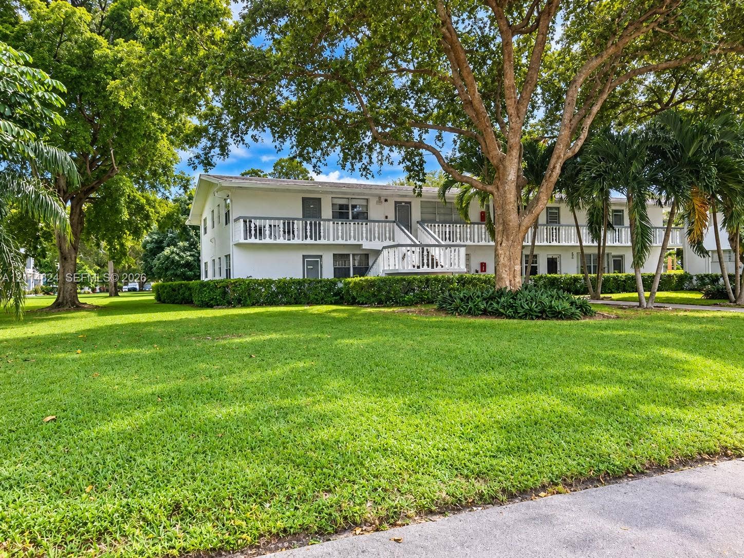 563 Durham T, #563, Deerfield Beach, FL 33442 Two-story exterior featuring white stucco siding, expansive wrap-around balconies with railings, mature shade trees, and manicured landscaping