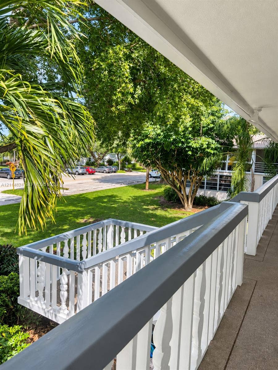 563 Durham T, #563, Deerfield Beach, FL 33442 Covered balcony with a gray-painted wood railing, featuring balusters and a concrete floor surface overlooking a landscaped lawn with mature trees and palms