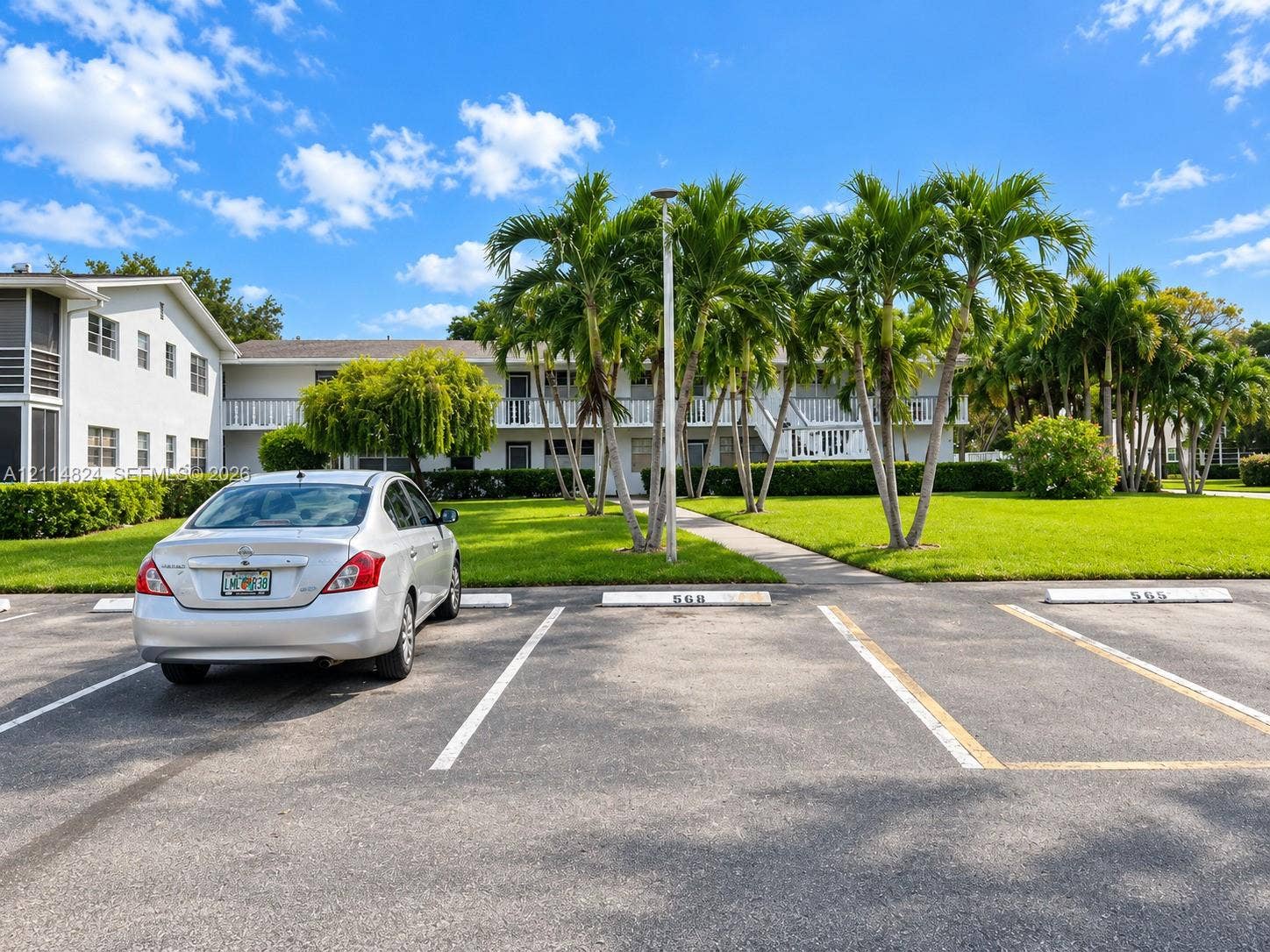 563 Durham T, #563, Deerfield Beach, FL 33442 Two-story exterior featuring a light-colored facade, private balconies with railings, mature palm trees, and an asphalt parking area with designated numbered spaces