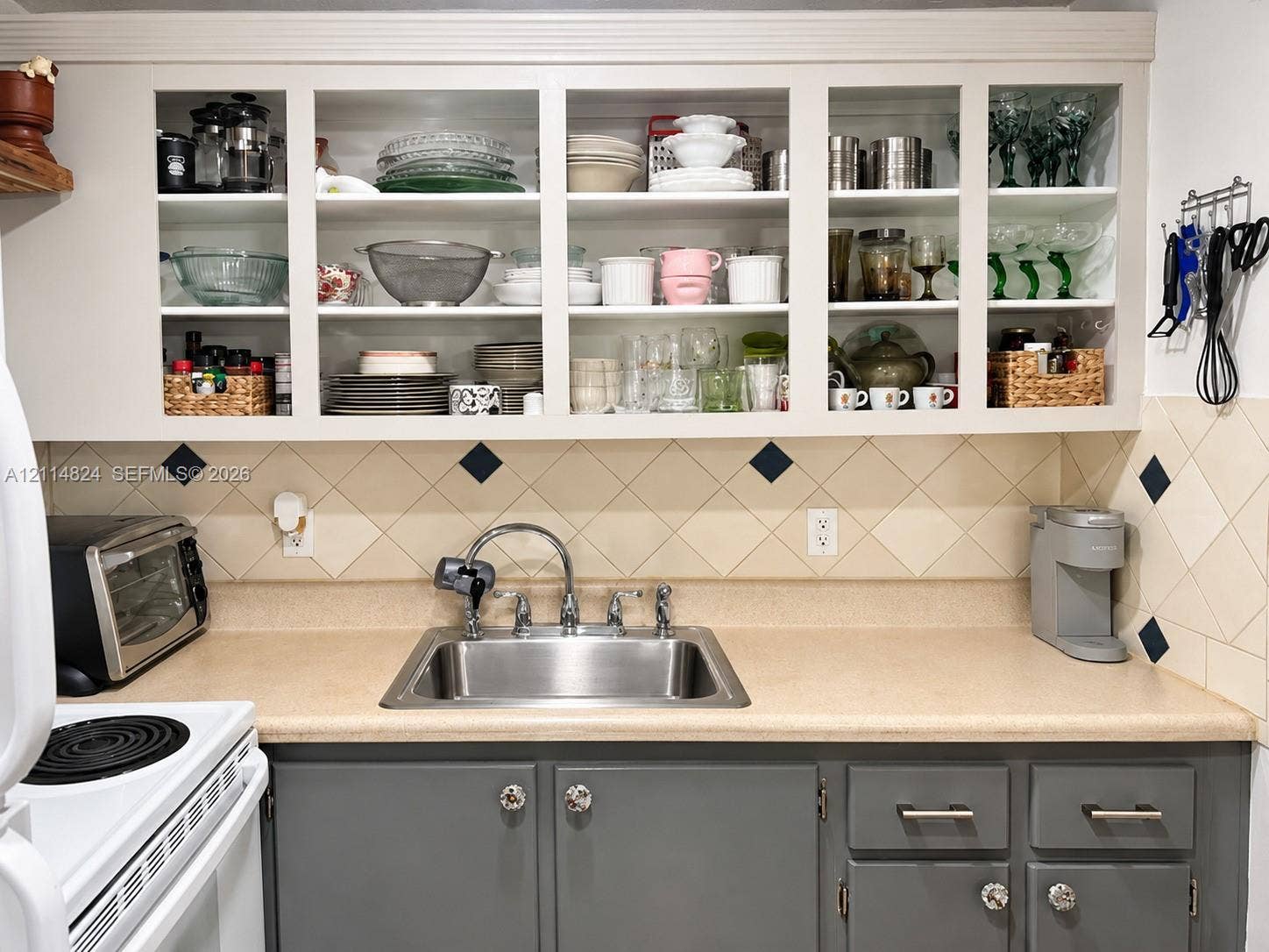 563 Durham T, #563, Deerfield Beach, FL 33442 Kitchen featuring grey lower cabinetry with metallic hardware, solid-surface countertops, a stainless steel undermount sink, and glass-front upper cabinets with integrated shelving