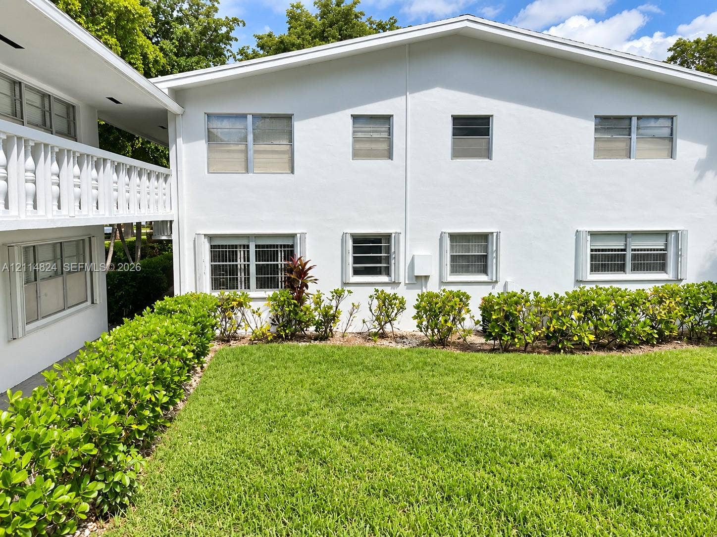 563 Durham T, #563, Deerfield Beach, FL 33442 Multi-story exterior featuring white stucco finish, second-level balcony with decorative railings, manicured lawn, and established hedge landscaping