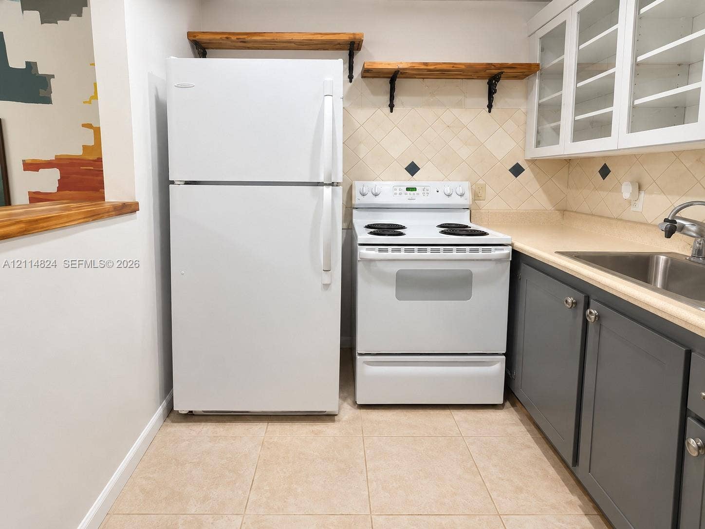 563 Durham T, #563, Deerfield Beach, FL 33442 Kitchen featuring charcoal shaker-style cabinetry, white appliances, wall-mounted wood shelving, diamond-patterned tile backsplash with inset accents, and tile flooring