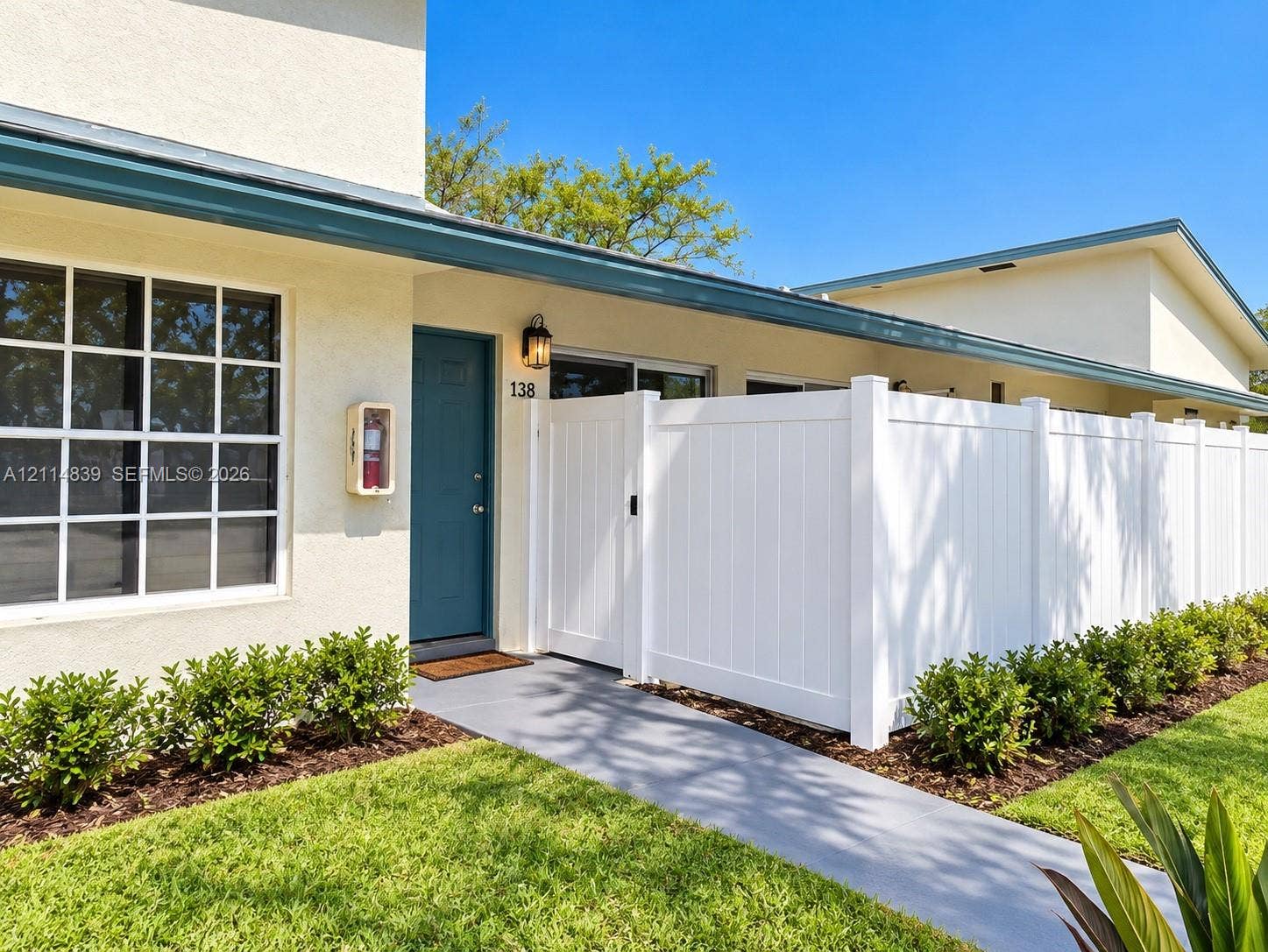 3000 NW 5th Terrace, #131, Pompano Beach, Pompano Beach, FL 33064 Exterior facade featuring smooth stucco finish, grid-pane windows, covered entryway with wall-mounted lighting, and a white vinyl privacy fence