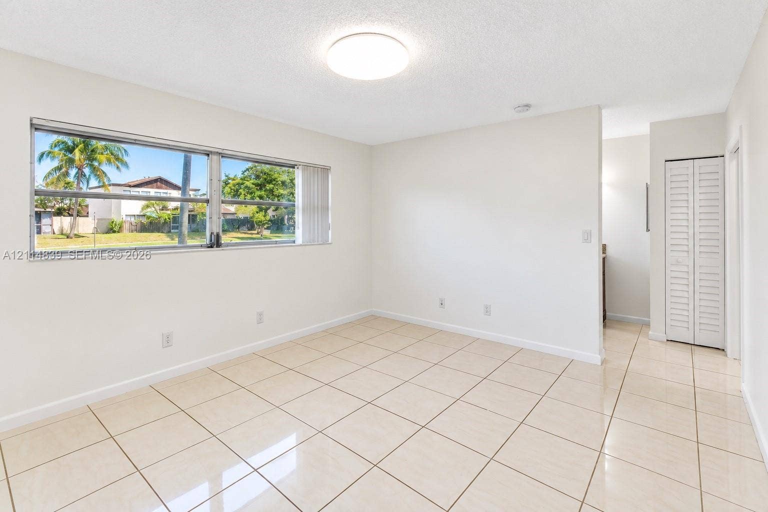 3000 NW 5th Terrace, #131, Pompano Beach, Pompano Beach, FL 33064 Neutral-toned interior featuring large-format tile flooring, oversized horizontal sliding window, flush-mount ceiling light, and built-in closet with louvered doors