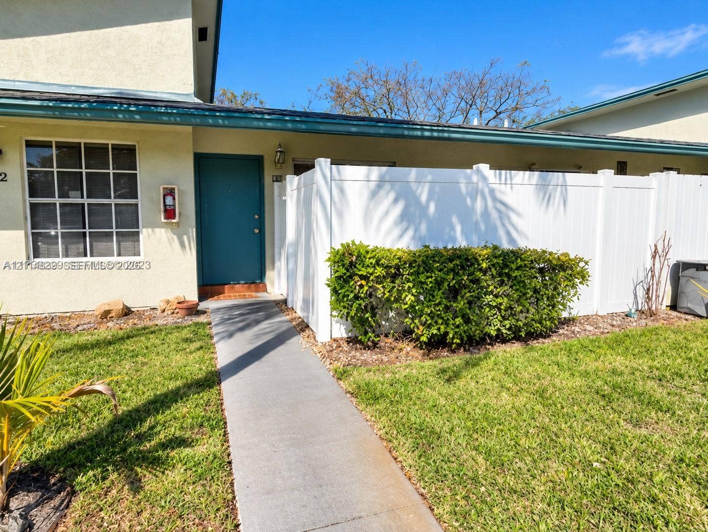 3000 NW 5th Terrace, #131, Pompano Beach, Pompano Beach, FL 33064 Exterior entrance featuring a solid door, concrete walkway, white privacy fencing, and maintained shrubbery