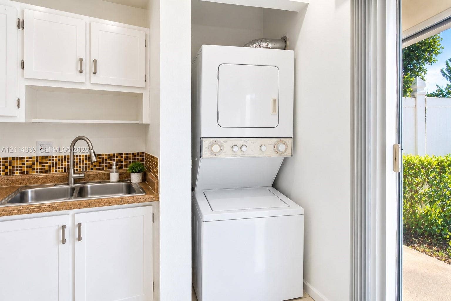 3000 NW 5th Terrace, #131, Pompano Beach, Pompano Beach, FL 33064 Laundry area featuring white cabinetry, a double-basin stainless steel sink, a mosaic tile backsplash, and a stacked washer-dryer unit