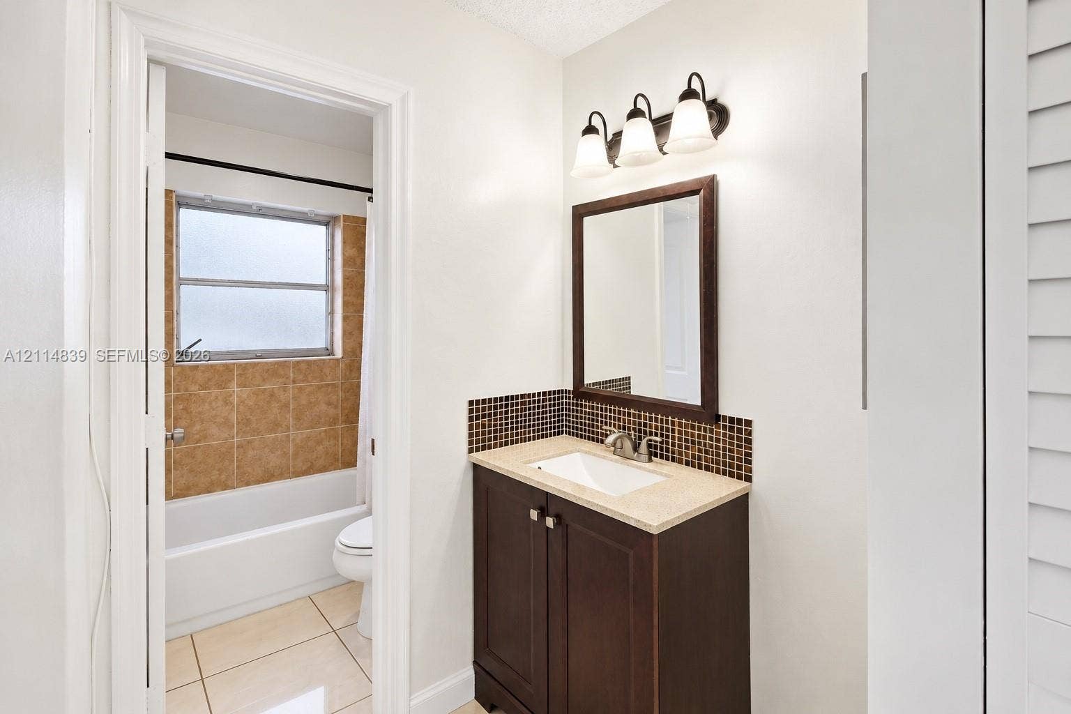 3000 NW 5th Terrace, #131, Pompano Beach, Pompano Beach, FL 33064 Bathroom featuring a dark wood-finish vanity with an integrated basin, stone-composite countertop, mosaic tile backsplash, and a three-light wall-mounted fixture