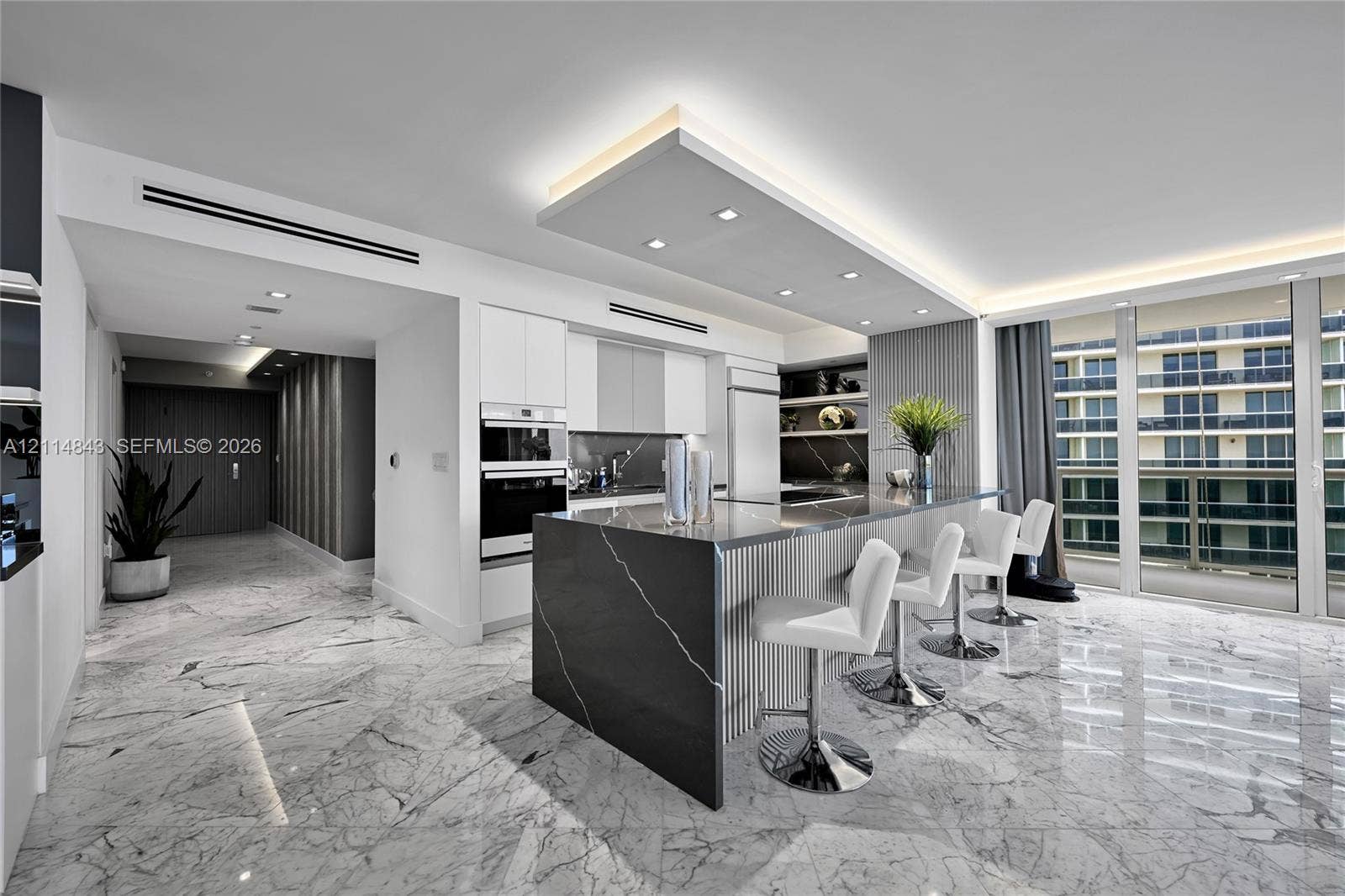 Kitchen featuring a central island with a stone countertop and waterfall edge, flat-panel cabinetry, a built-in wall oven, recessed ceiling lighting, and stone-finish flooring