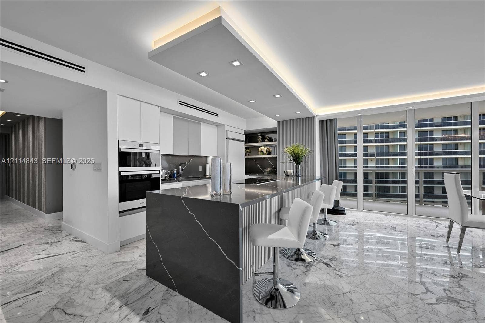 Kitchen featuring a waterfall-edge stone island, built-in dual ovens, recessed tray ceiling lighting, stone flooring, and floor-to-ceiling windows