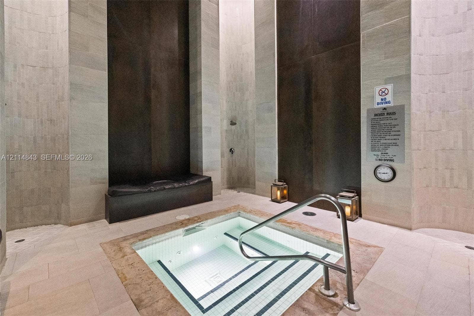 Indoor spa featuring a tiled plunge pool with metal handrail, stone tile walls, built-in bench seating, and an integrated shower head