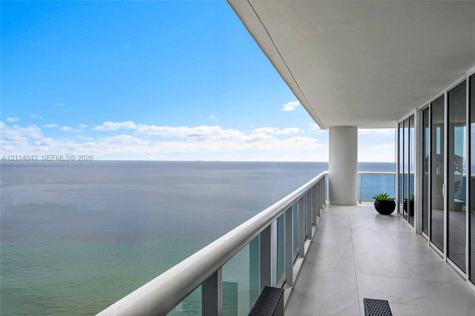Covered balcony featuring oversized tile flooring, a glass panel railing, and expansive ocean scenery
