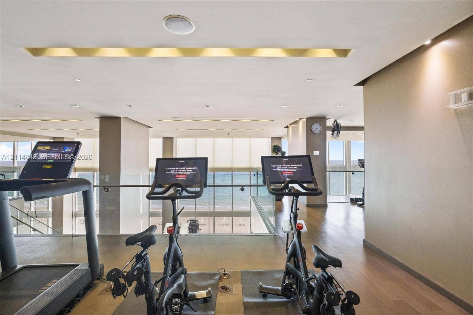 Fitness area featuring wood-finish flooring, recessed ceiling lighting, glass railings, and expansive windows with ocean scenery