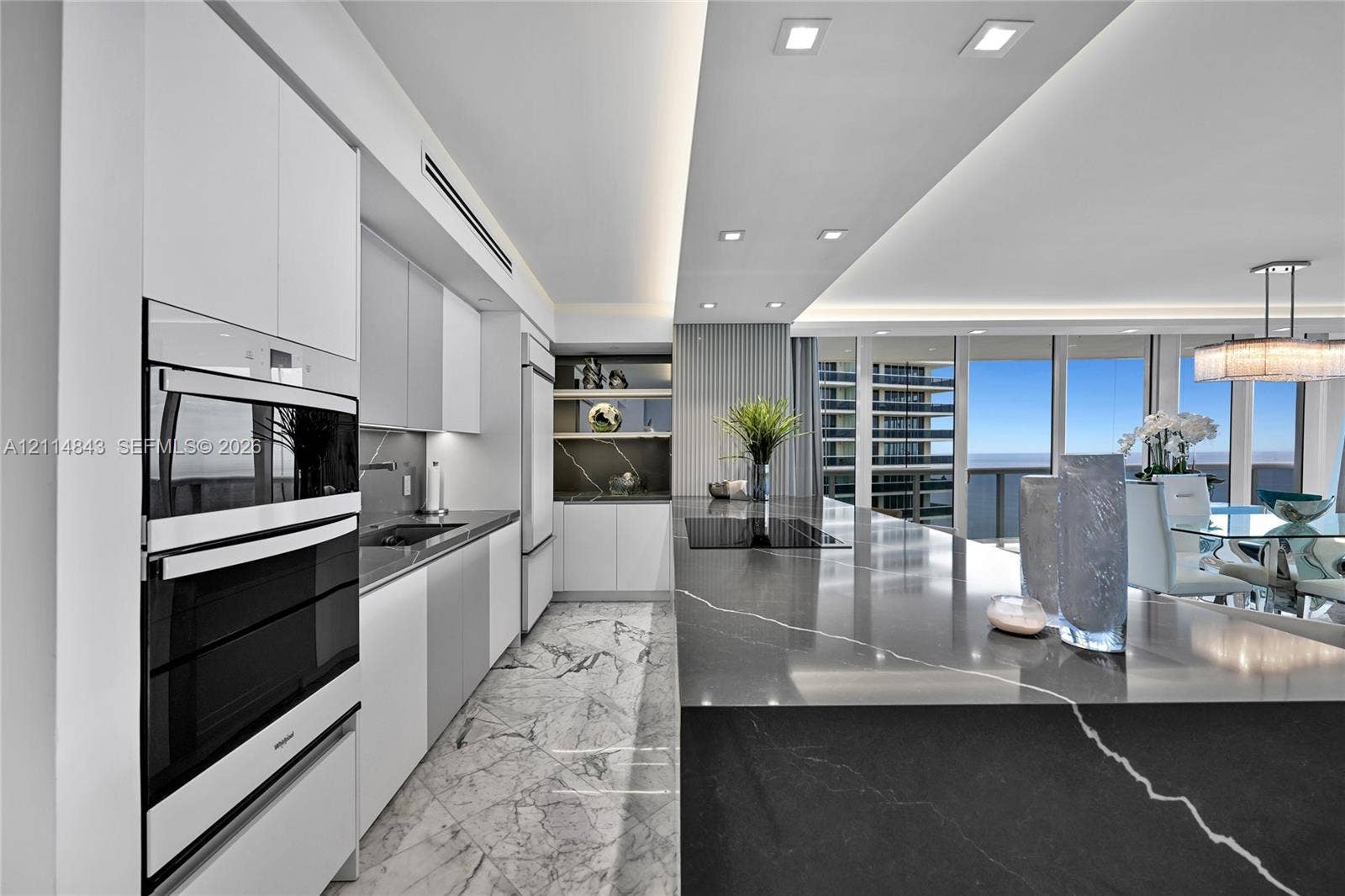 Kitchen featuring high-gloss cabinetry, stone-finish countertops, integrated double wall ovens, recessed ceiling lighting, and floor-to-ceiling windows