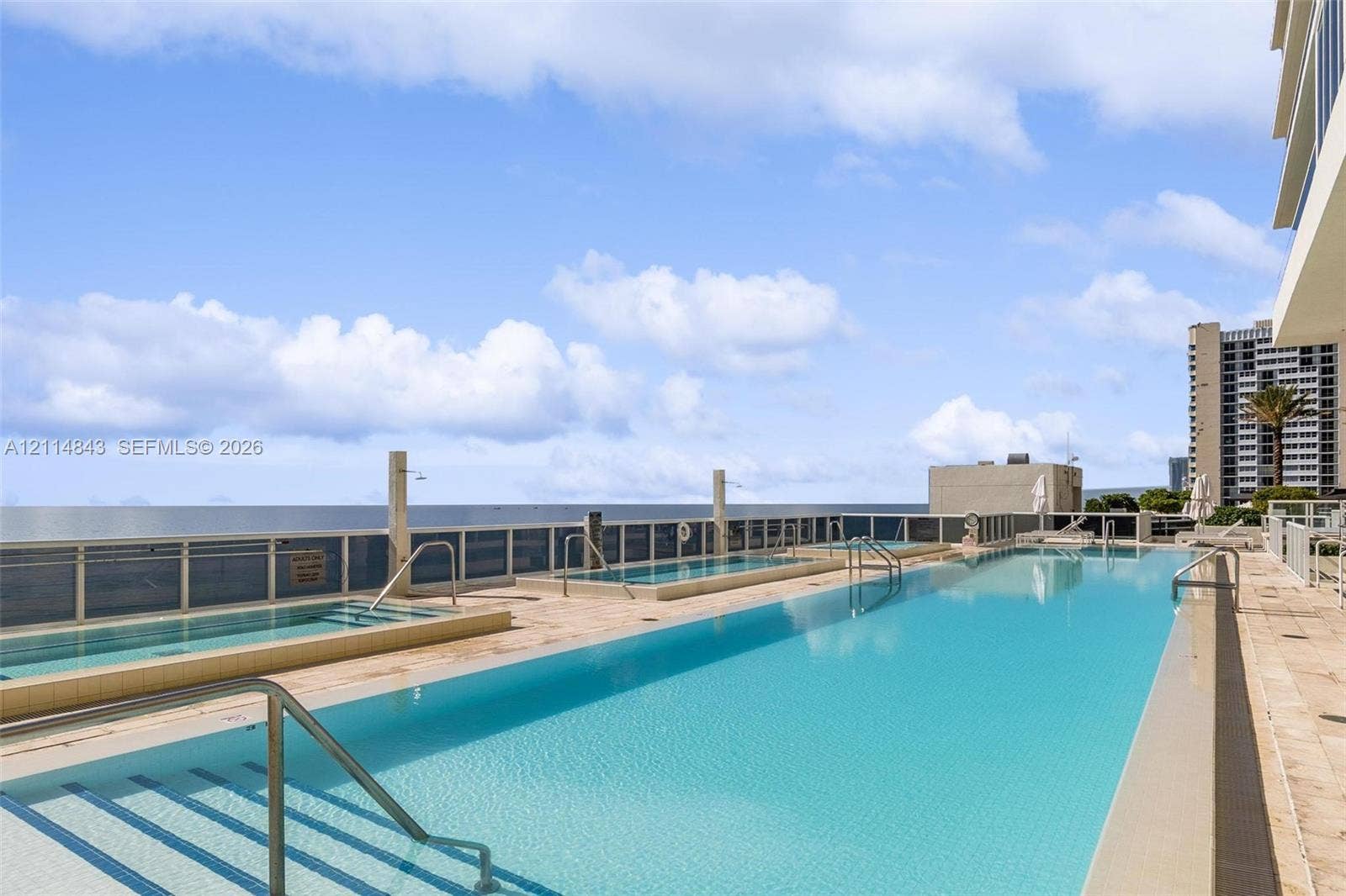 Rooftop terrace featuring an expansive lap pool, multiple recessed spa basins, natural stone decking, and a glass panel perimeter railing