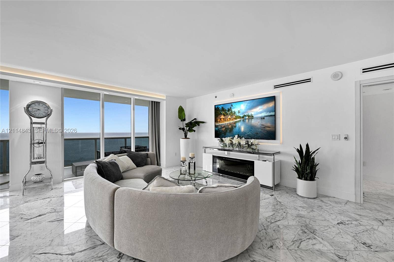 Open-concept living space featuring floor-to-ceiling glass windows, polished stone flooring, recessed ceiling accent lighting, and a built-in electric fireplace with surrounding wall niche
