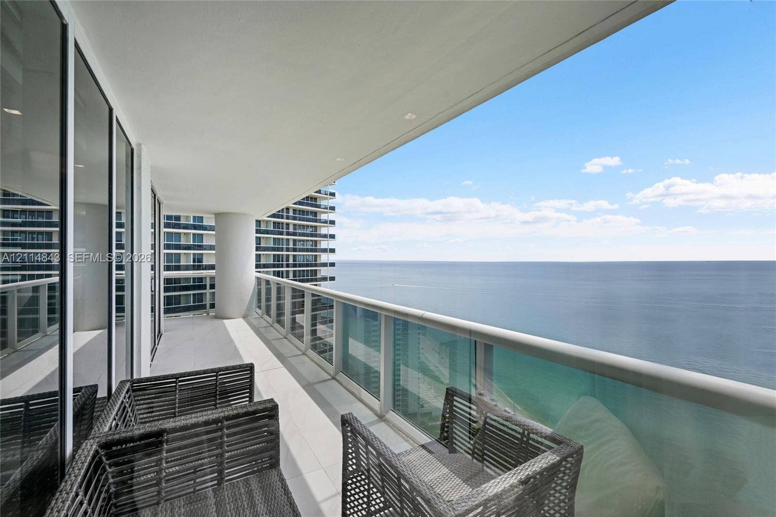 Covered private balcony with tile flooring, glass panel railing, and metal handrail