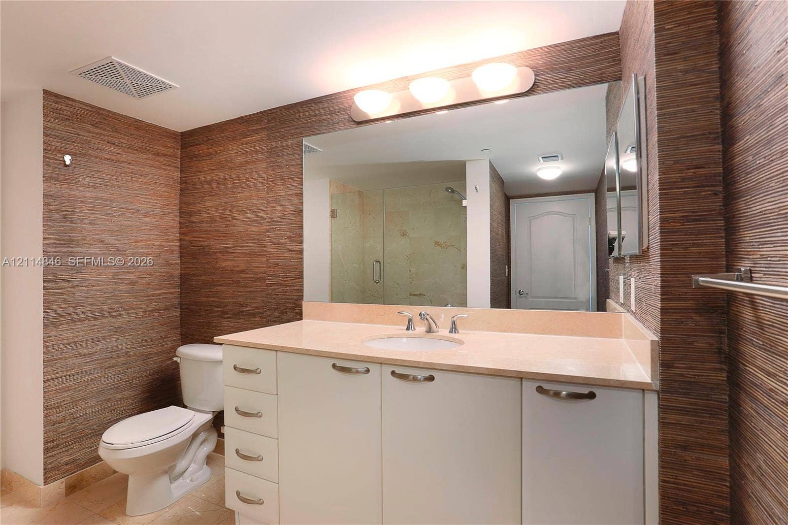 2101 Brickell Avenue, #601, Miami, Miami, FL 33129 Bathroom featuring textured wall covering, a neutral-toned countertop with an integrated basin, white cabinetry with metallic hardware, and a large wall-mounted mirror
