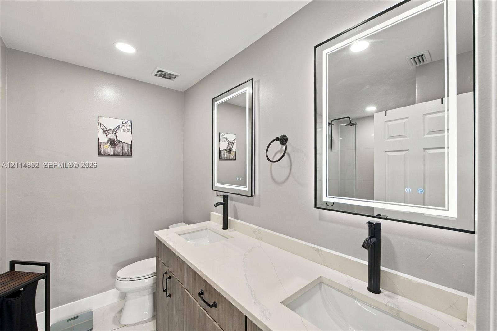 10780 NW 10th Street, Plantation, FL 33322 Double vanity featuring a light-toned countertop, dual rectangular undermount sinks, matte black tall-spout faucets, and rectangular backlit mirrors