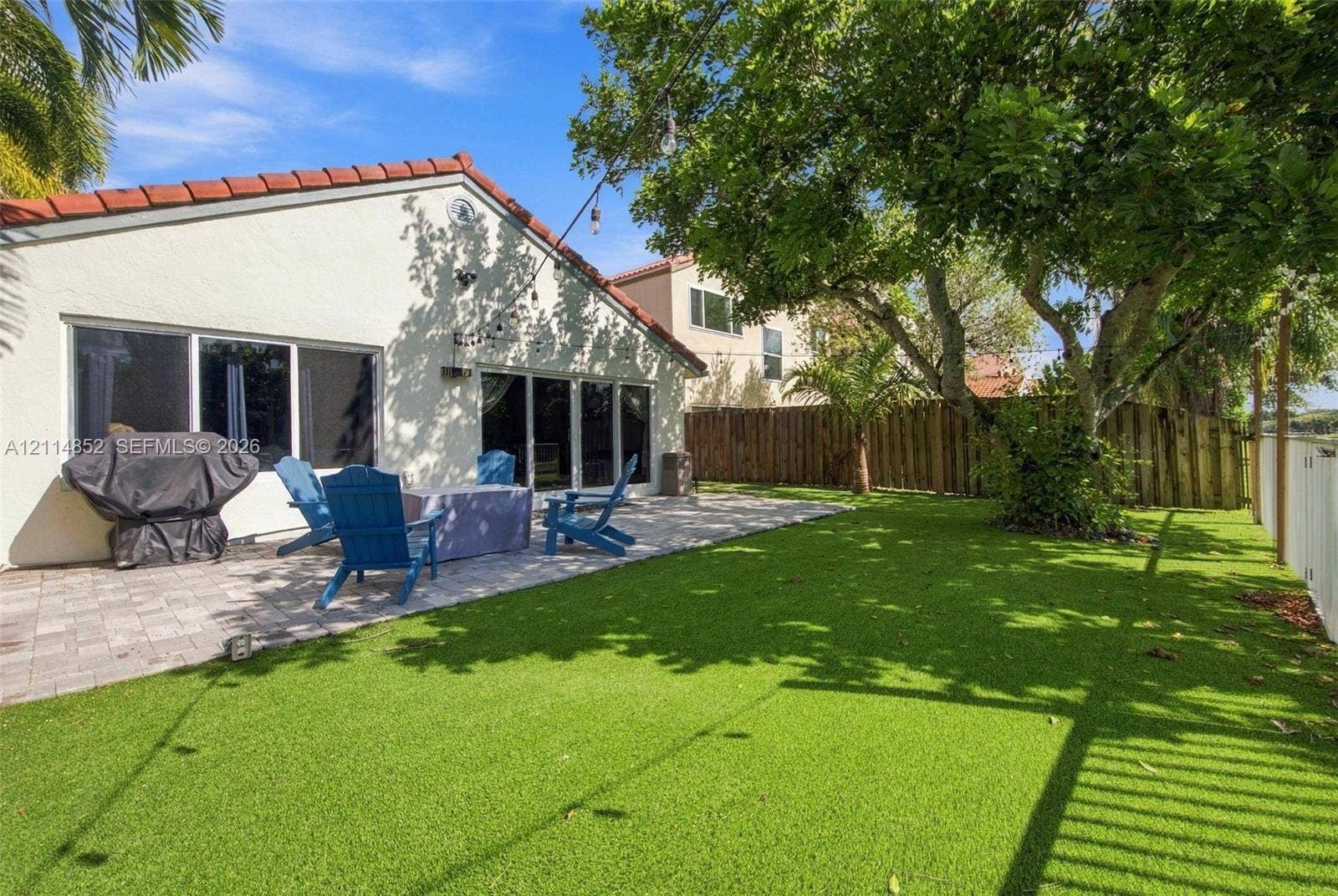10780 NW 10th Street, Plantation, FL 33322 Backyard featuring a paved stone patio, synthetic lawn, and mature trees, enclosed by perimeter fencing