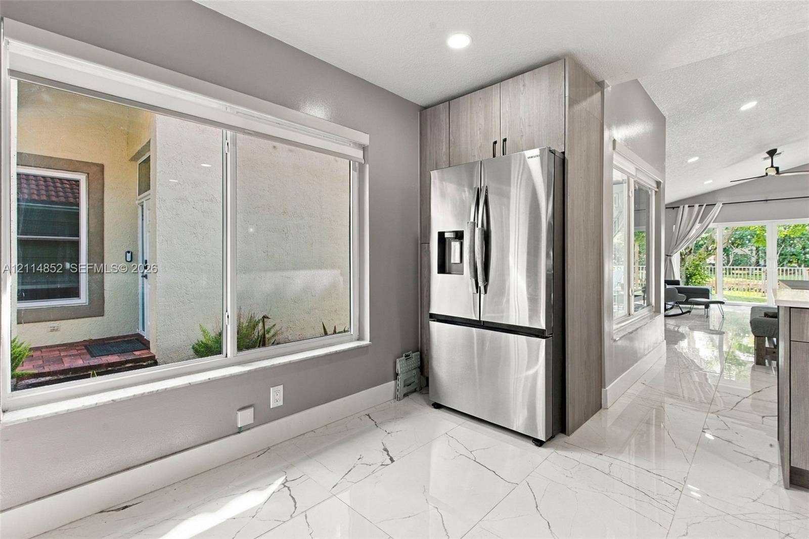 10780 NW 10th Street, Plantation, FL 33322 Large picture window, stainless steel French-door refrigerator, floor-to-ceiling wood-finish cabinetry, and polished stone-finish tile flooring with veining