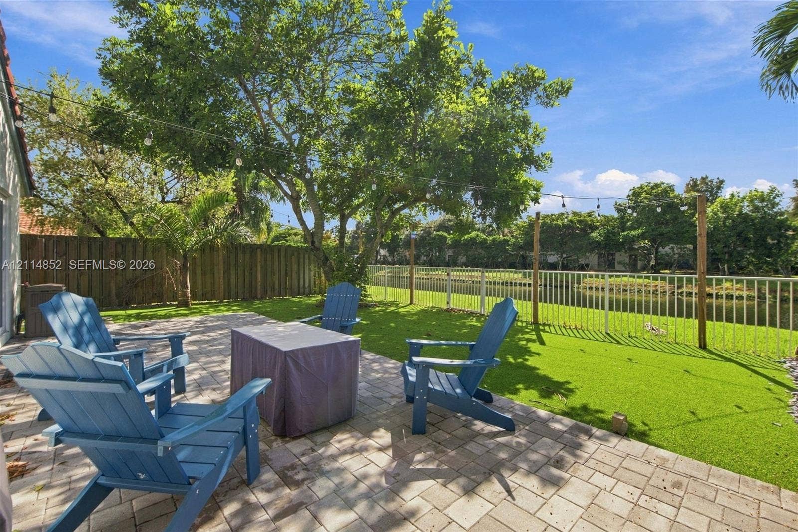 10780 NW 10th Street, Plantation, FL 33322 Backyard featuring a paved patio, perimeter wood fencing, water-facing white metal fencing, mature trees, and string lighting