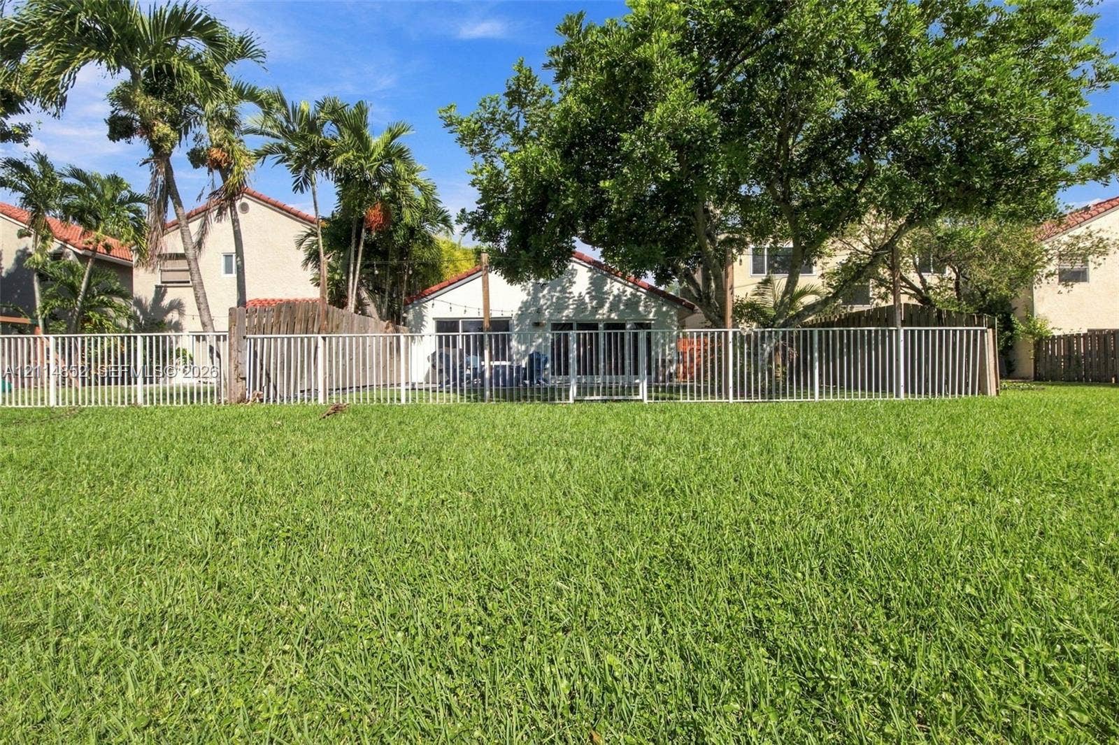 10780 NW 10th Street, Plantation, FL 33322 Expansive backyard featuring a manicured lawn, white metal fencing, mature trees, and palm trees