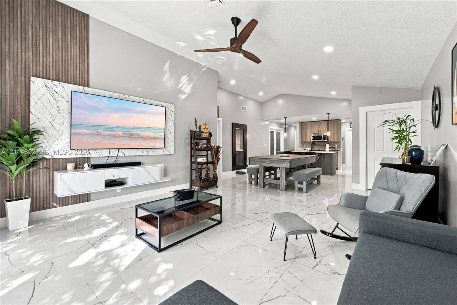 10780 NW 10th Street, Plantation, FL 33322 Open-concept living space featuring high vaulted ceilings, large-format polished tile flooring, a vertical wood-slat accent wall, and a custom wall-mounted floating media console with stone-finish cladding