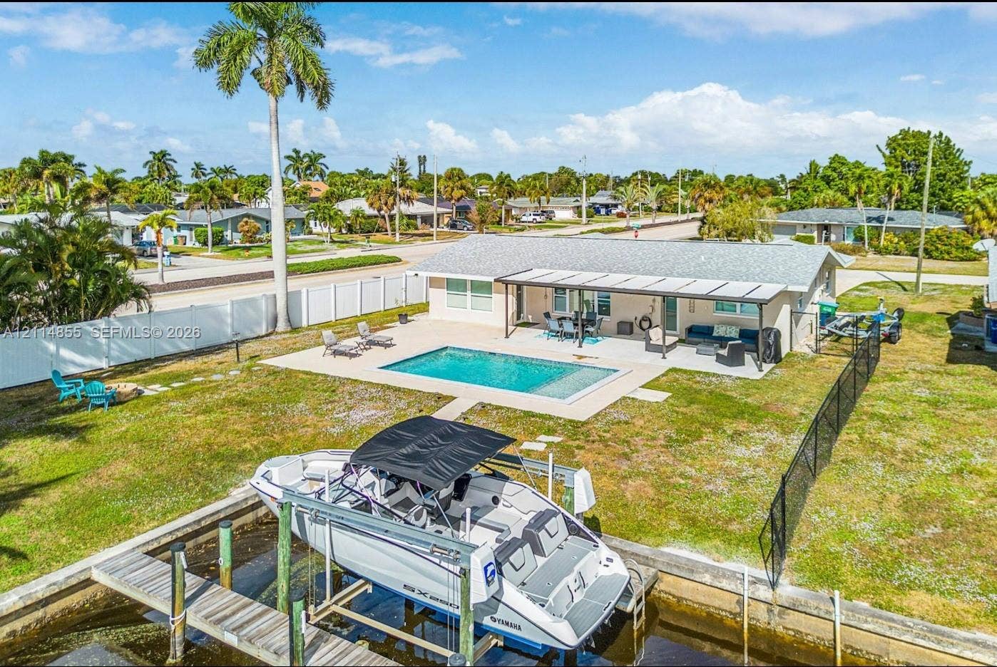 802 Montclair Court, Cape Coral, FL 33904 Waterfront property featuring a private boat lift, a swimming pool, a covered concrete patio, and perimeter fencing