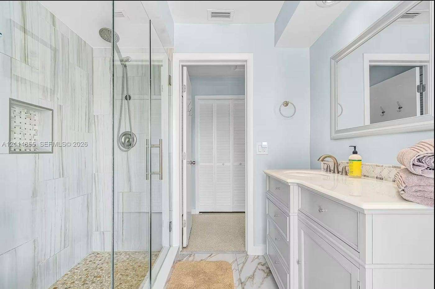 802 Montclair Court, Cape Coral, FL 33904 Walk-in glass-enclosed shower with a rainfall showerhead, integrated tiled wall niche, pebble stone flooring, stone-finish wall tile, and a single-sink vanity with a light-toned countertop