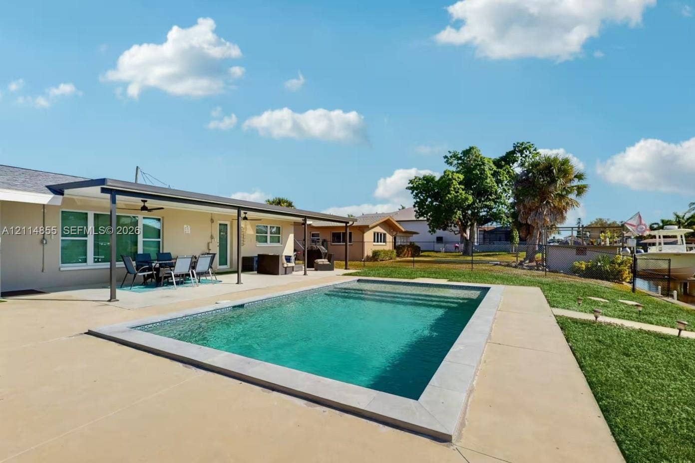 802 Montclair Court, Cape Coral, FL 33904 In-ground pool featuring a stone border, expansive concrete patio, and a covered lanai with ceiling fans