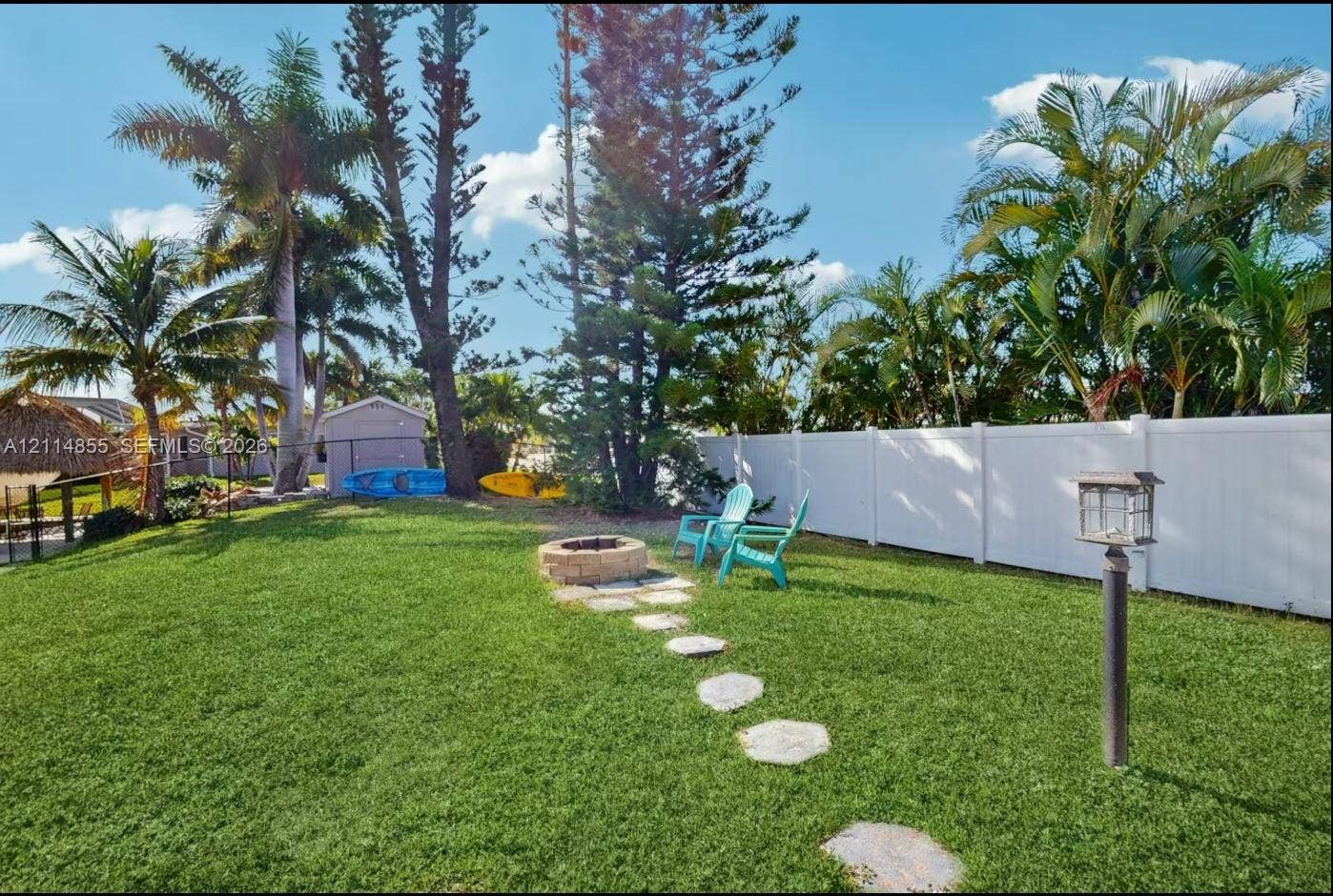 802 Montclair Court, Cape Coral, FL 33904 Fenced backyard featuring a manicured lawn, stone-paver path, stone fire pit, and mature palm trees