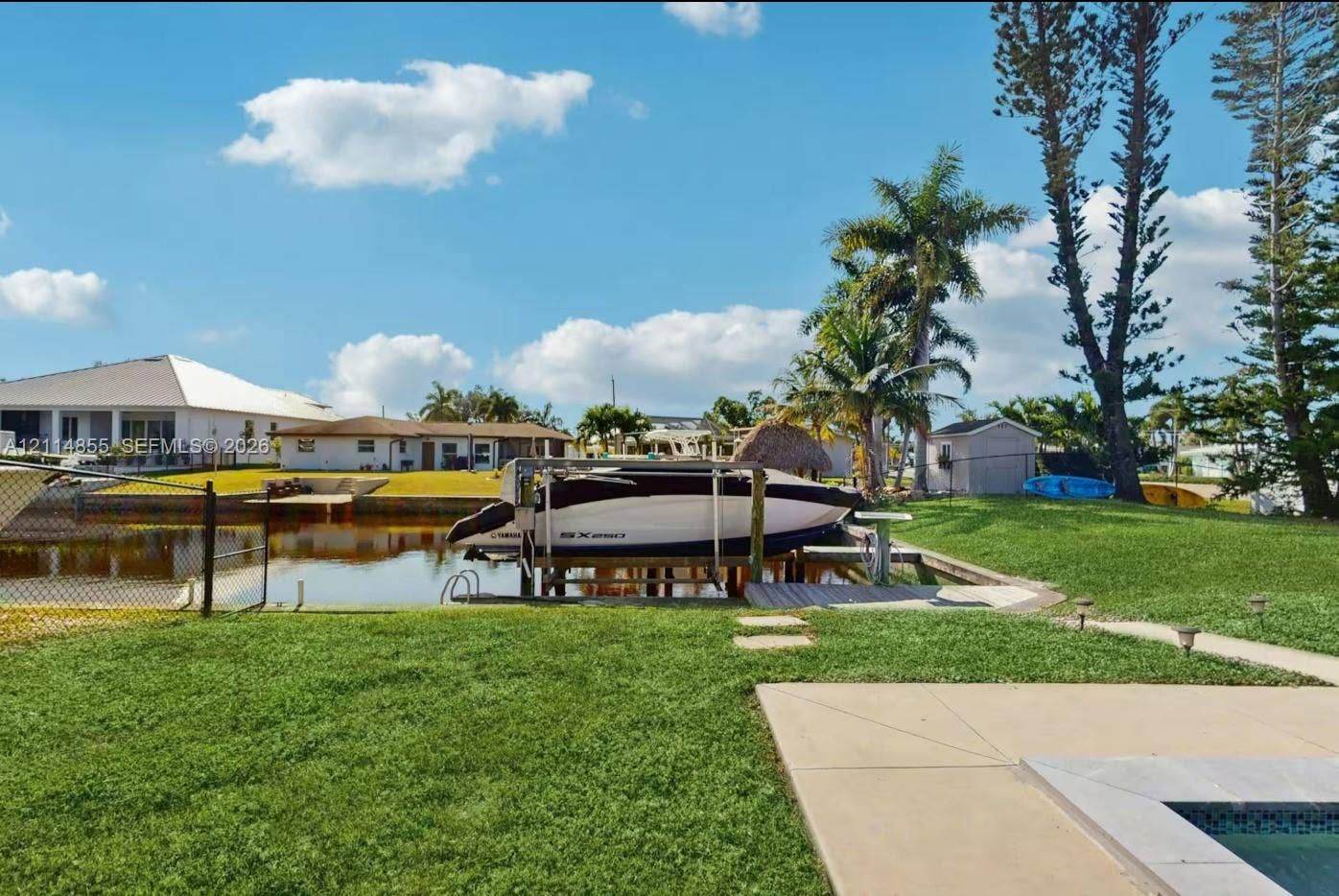 802 Montclair Court, Cape Coral, FL 33904 Waterfront backyard featuring a private boat lift, a canal bulkhead, an expansive lawn, and a concrete patio