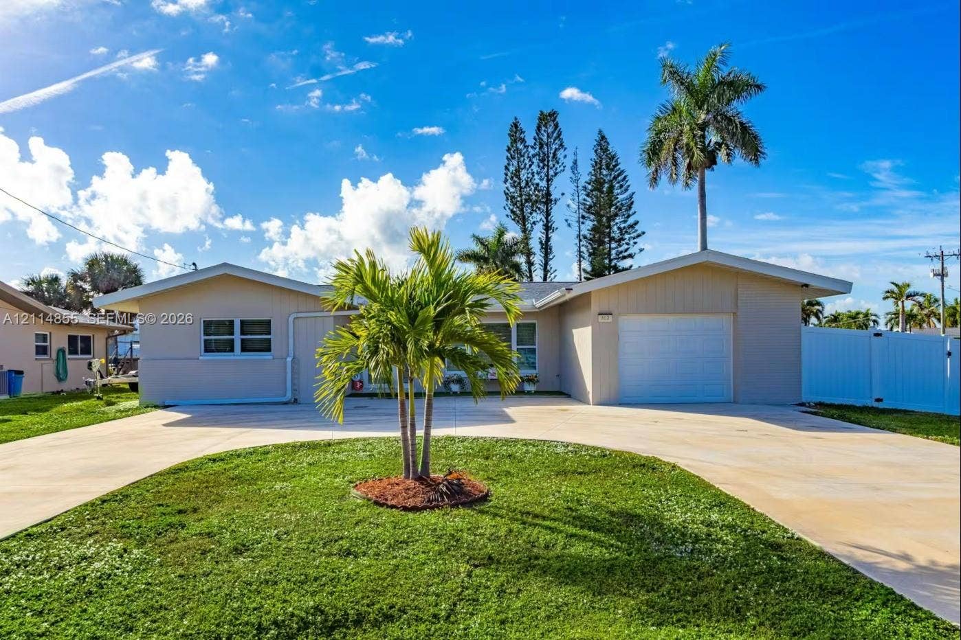 802 Montclair Court, Cape Coral, FL 33904 Single-story residence featuring a stucco exterior, concrete driveway, attached garage, and landscaping with mature palm trees