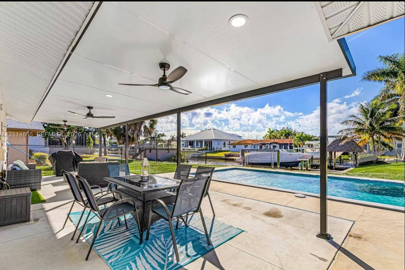 802 Montclair Court, Cape Coral, FL 33904 Covered outdoor patio featuring a concrete floor, recessed ceiling lighting, and two ceiling fans, overlooking an in-ground swimming pool and canal frontage