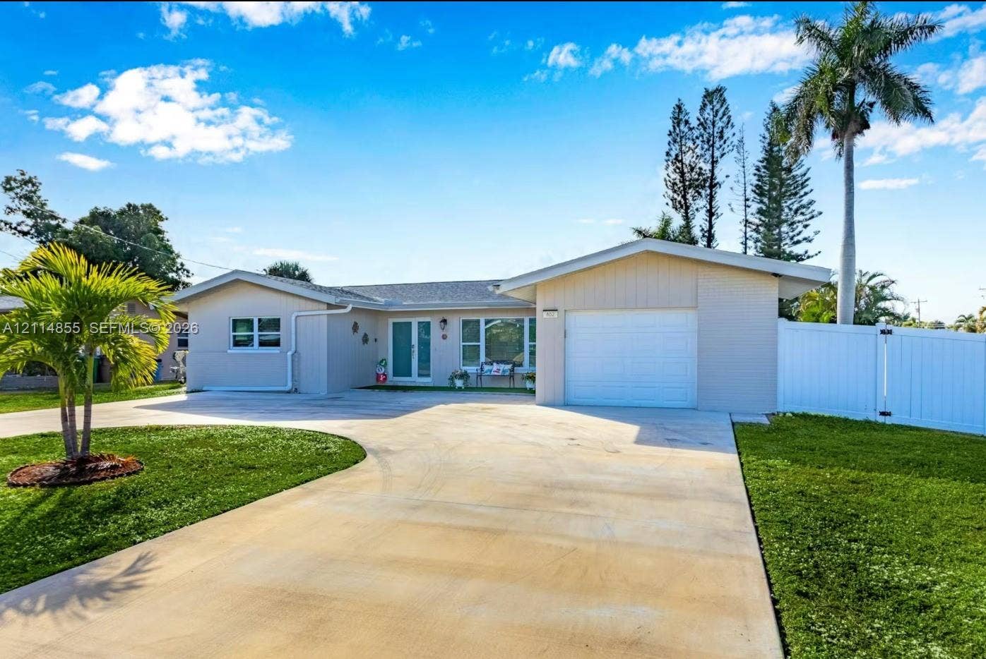 802 Montclair Court, Cape Coral, FL 33904 Single-story exterior featuring a concrete driveway, attached one-car garage, white vinyl fencing, and palm-accented landscaping