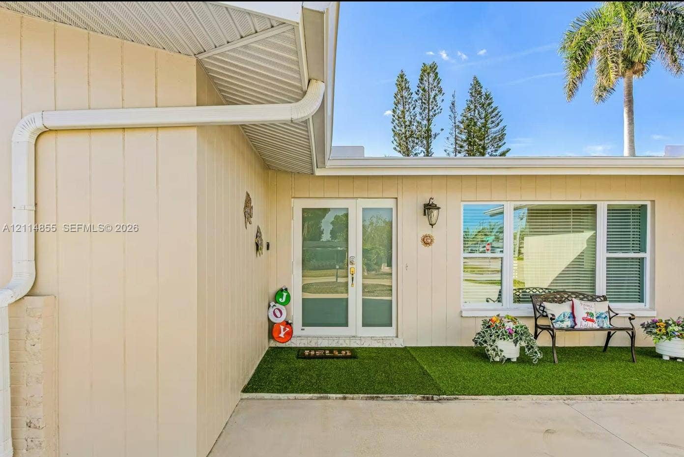 802 Montclair Court, Cape Coral, FL 33904 Exterior facade featuring light-toned vertical siding, double glass-panel entry doors, oversized triple-pane window, and an integrated outdoor porch area