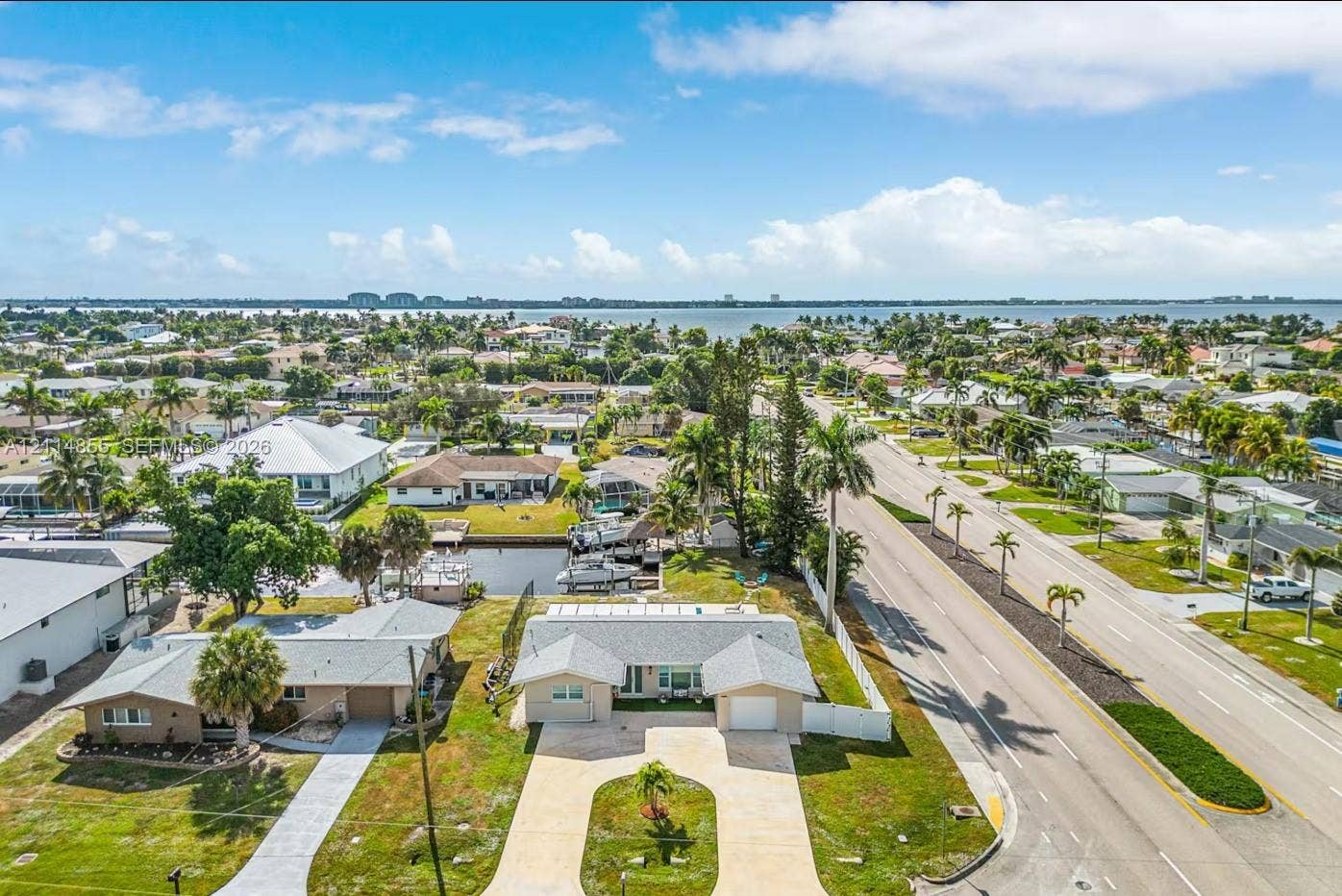 802 Montclair Court, Cape Coral, FL 33904 Aerial perspective featuring a single-story residence with a concrete driveway, attached garage, private canal access with boat dock, and surrounding tropical landscaping