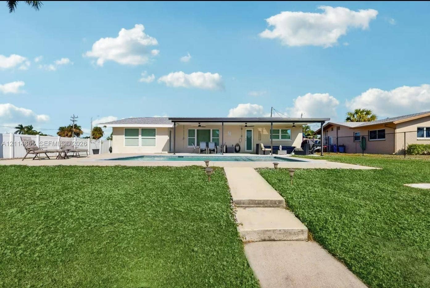 802 Montclair Court, Cape Coral, FL 33904 Exterior view featuring a rectangular swimming pool, concrete patio, expansive lawn, white vinyl fencing, and a covered porch with ceiling fans