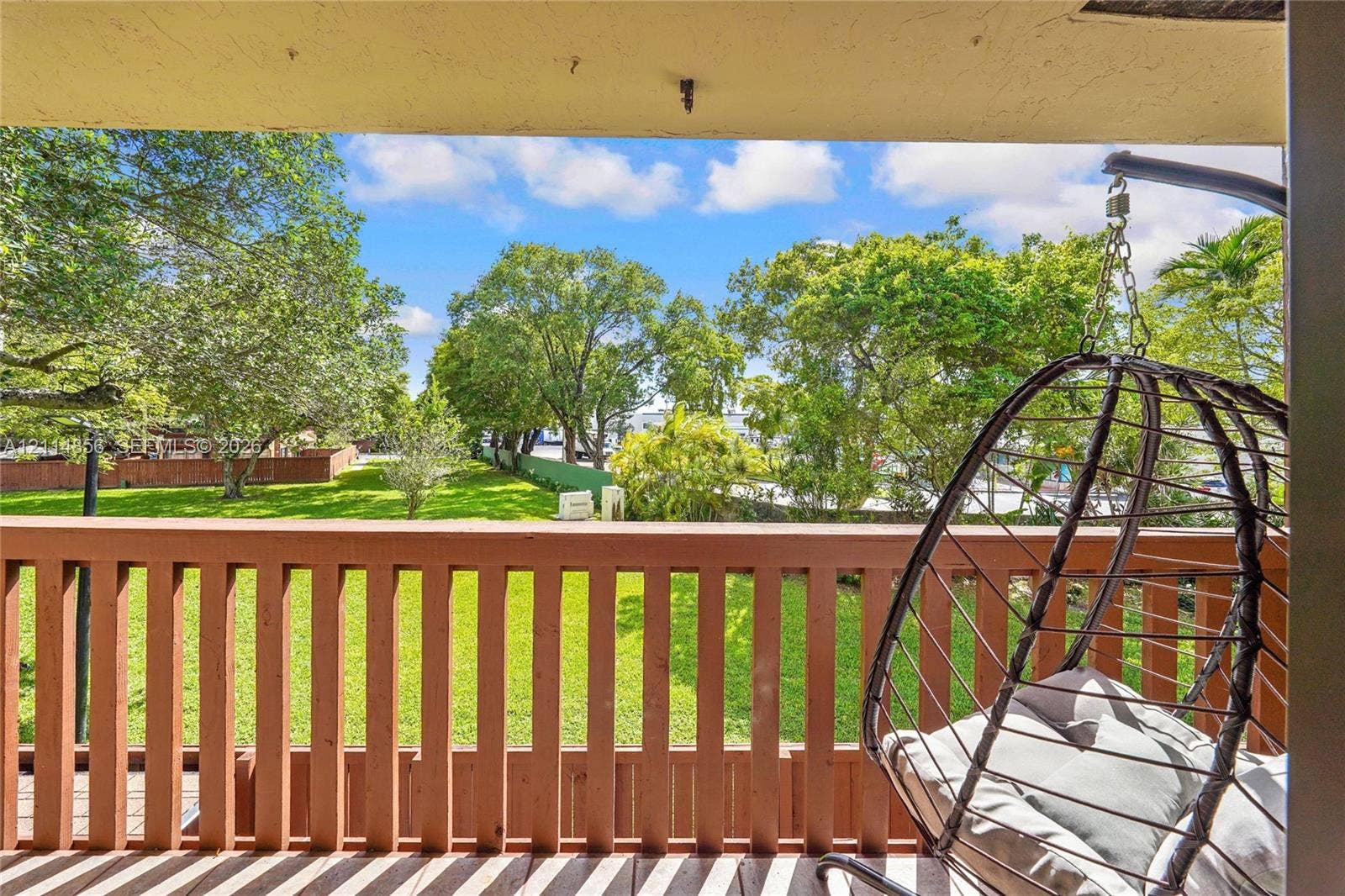 Miami, FL 33173 Covered balcony featuring a wood-style railing and an outdoor space overlooking a landscaped yard with mature trees