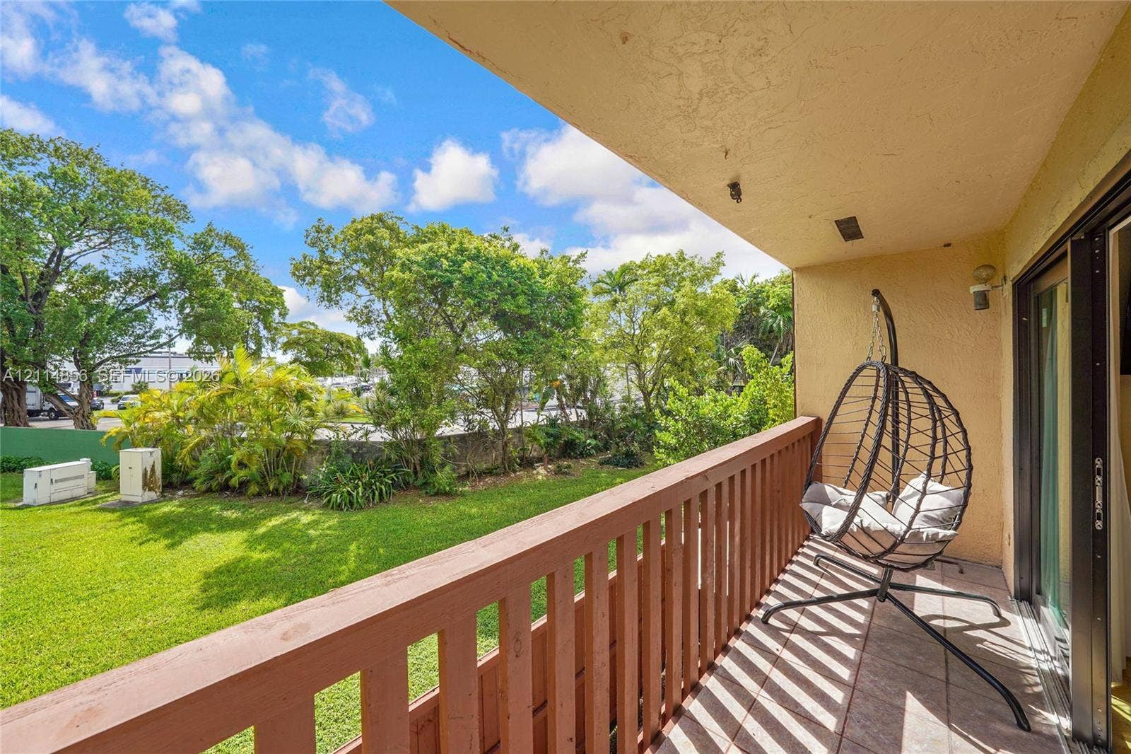 Miami, FL 33173 Covered balcony featuring wood-style railings, tile flooring, and direct access to a green space with mature landscaping