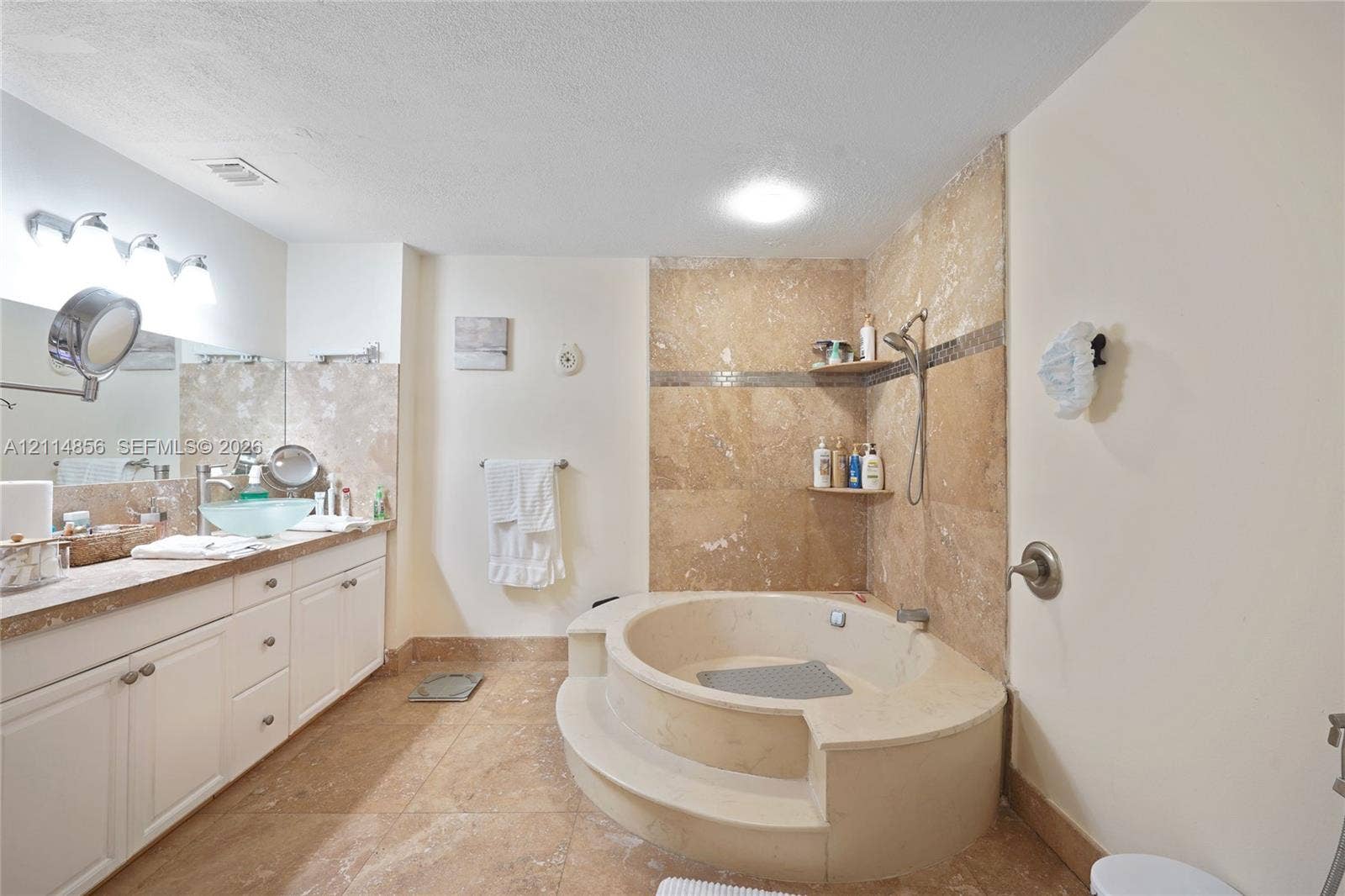 Miami, FL 33173 Bathroom featuring a stone-tile surround, circular soaking tub with a step-up entry, vanity with an integrated vessel sink, and stone-tile flooring