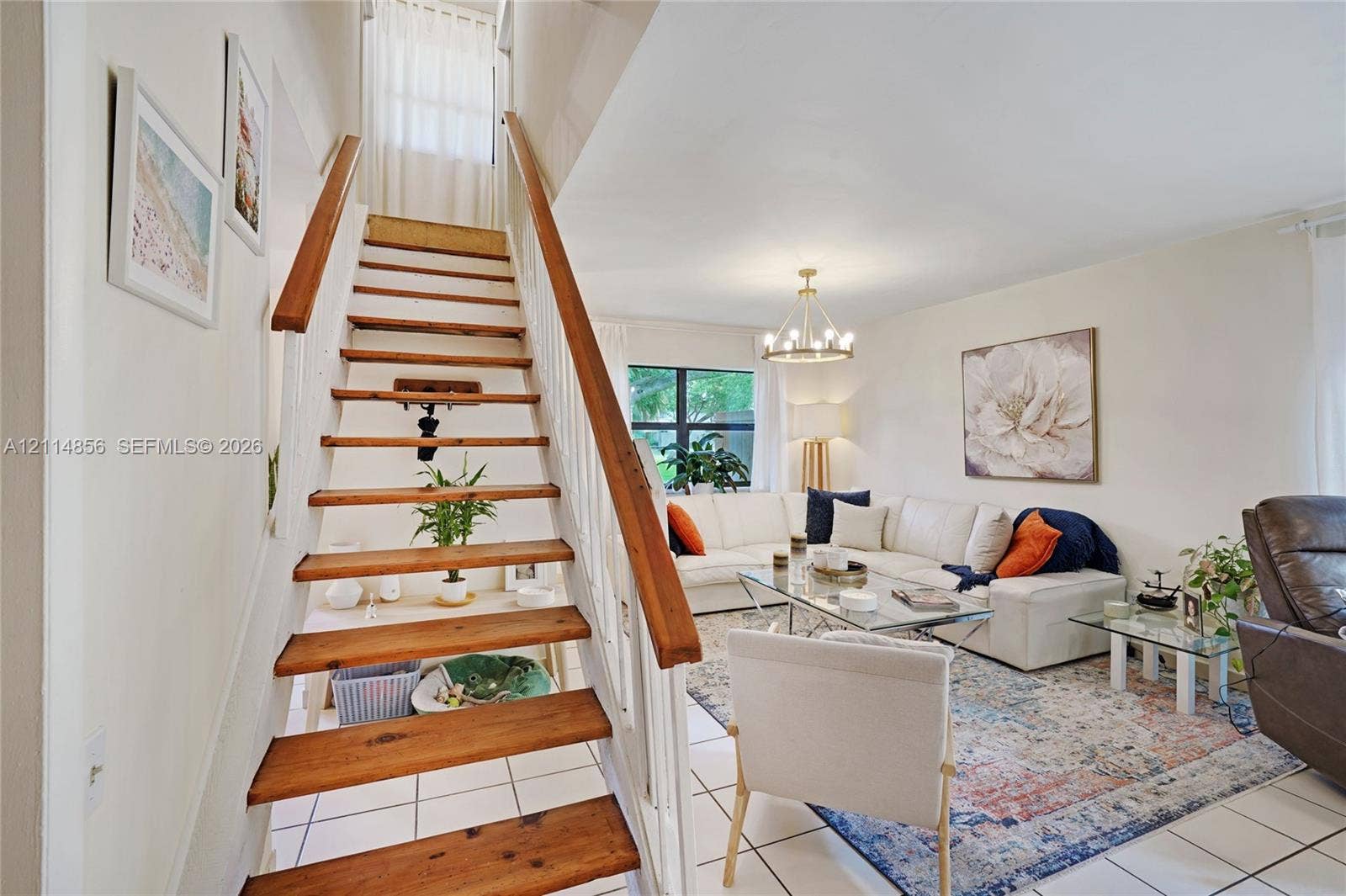 Miami, FL 33173 Open-concept living area featuring white tile flooring, wooden stair treads with white balusters, and a multi-arm modern chandelier