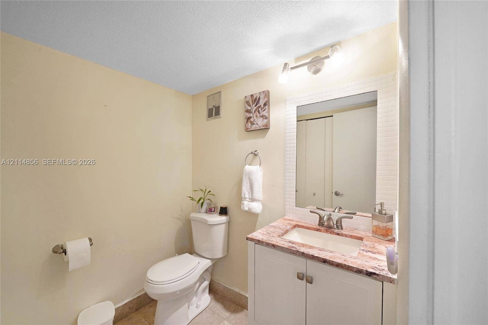 Miami, FL 33173 Vanity cabinet featuring stone countertop, integrated sink with dual-handle faucet, wall-mounted mirror, and multi-bulb light fixture