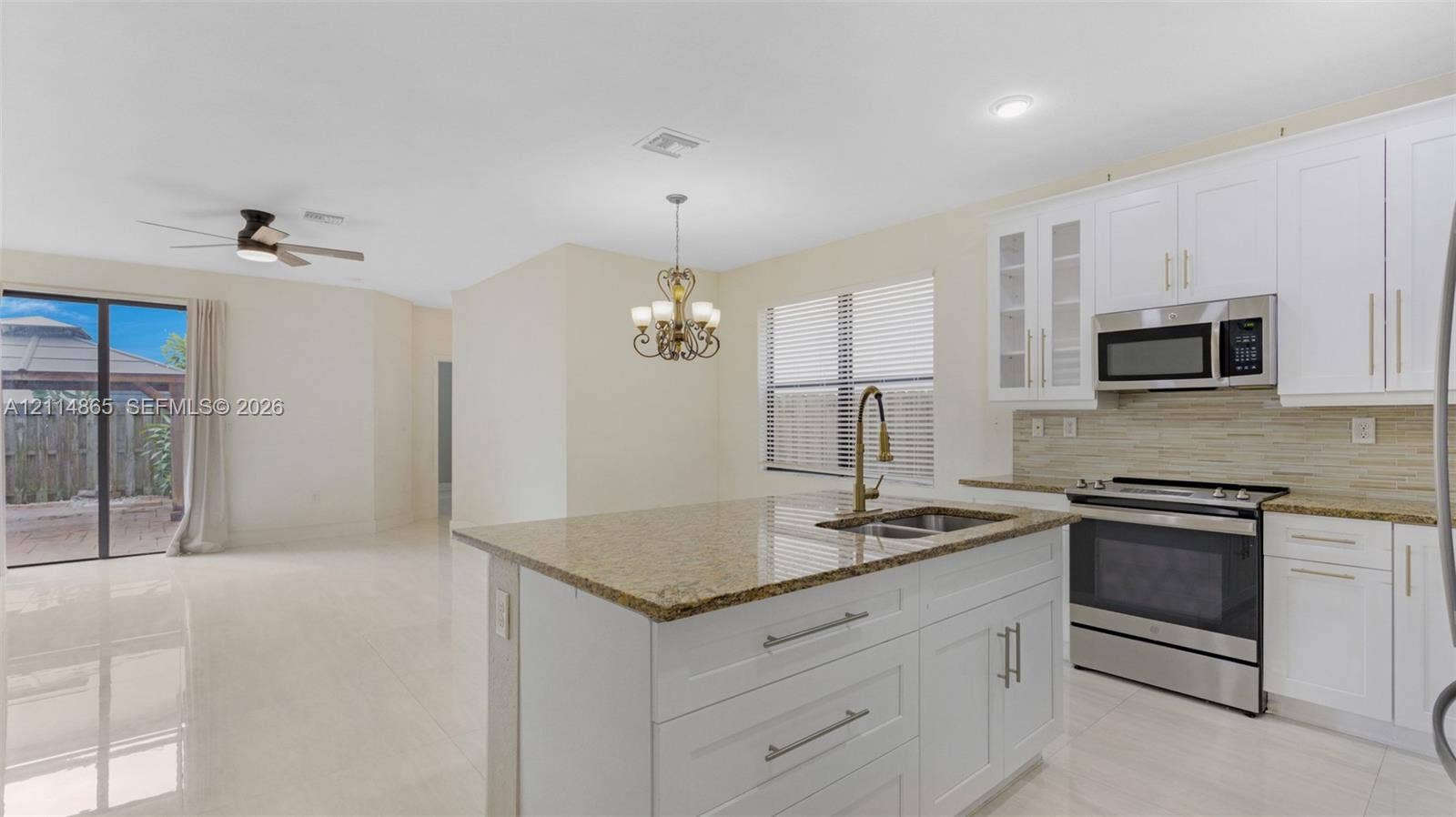 3754 NE 2nd Street, Homestead, FL 33033 Kitchen featuring white shaker-style cabinetry, stone-surface countertops, stainless steel appliances, a center island with an undermount sink, and tile flooring