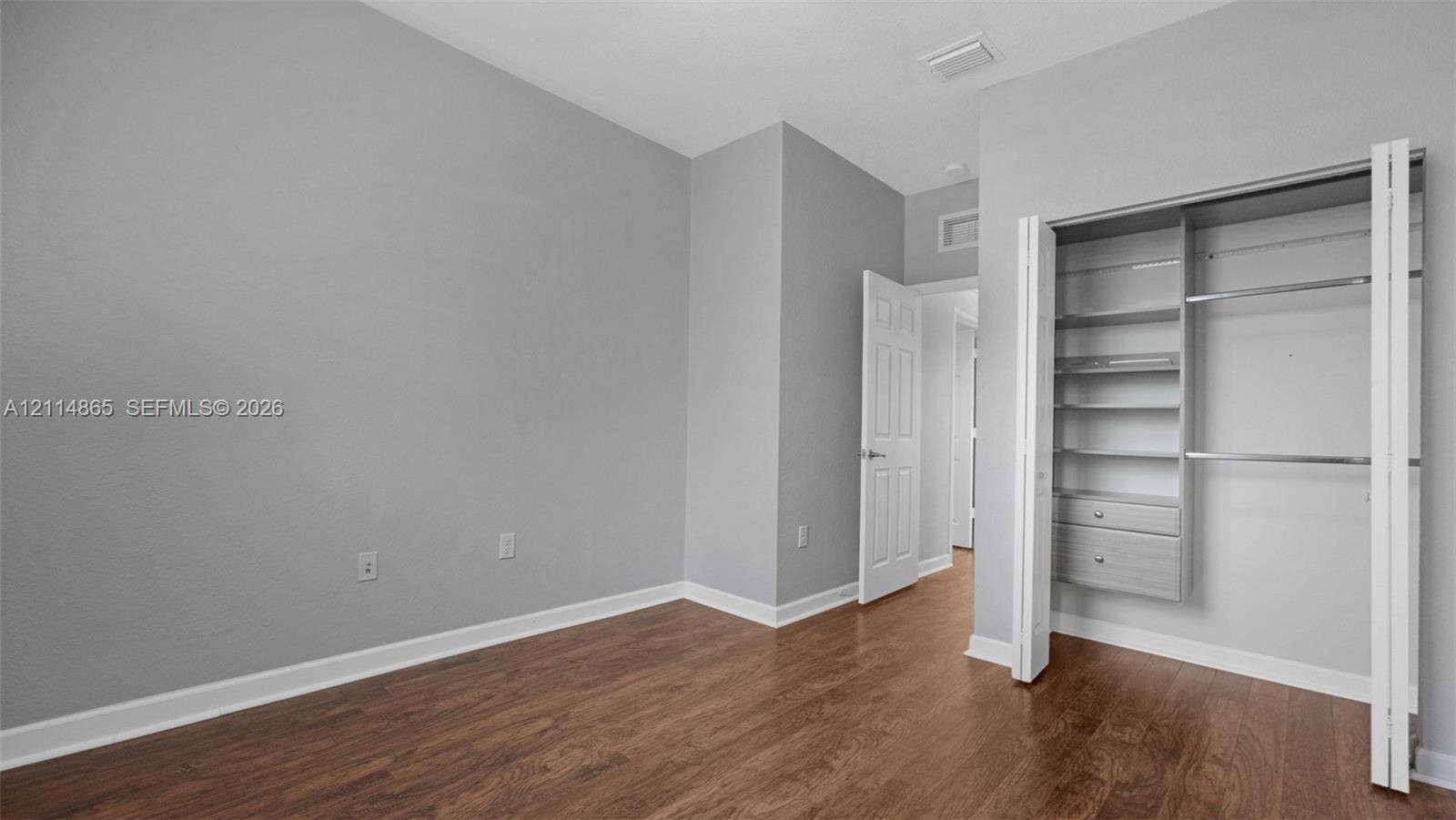 3754 NE 2nd Street, Homestead, FL 33033 Room featuring wood-finish flooring, neutral wall paint, and a built-in closet system with adjustable shelving and integrated drawers
