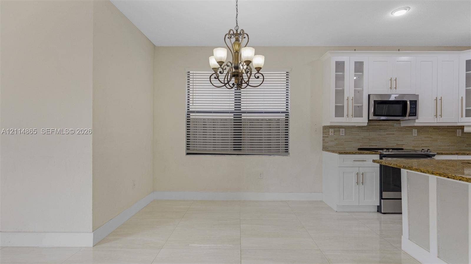 3754 NE 2nd Street, Homestead, FL 33033 Kitchen featuring white cabinetry with glass-panel accents, stone-finish countertops, stainless steel appliances, tile flooring, and a decorative chandelier