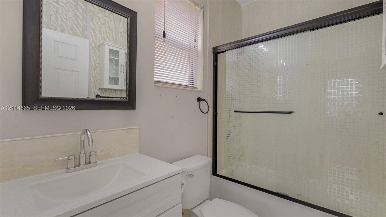 3754 NE 2nd Street, Homestead, FL 33033 Full guest bath, 1st floor! Bathroom featuring a vanity with a white countertop and integrated sink, a framed wall mirror, a white cabinet, and a bathtub with sliding glass doors and a dark frame